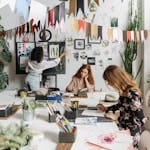 Artists paint in a bright, creative studio adorned with artwork and plants, fostering a vibrant atmosphere.