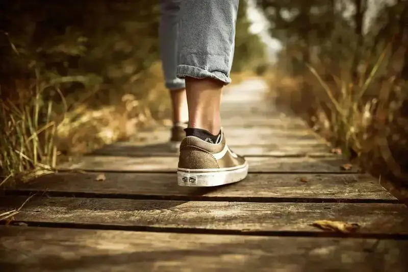 Une personne portant des baskets marchant sur un chemin en bois dans un parc ensoleillé.